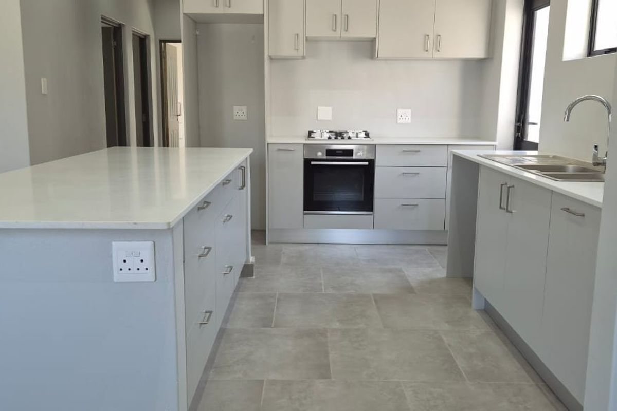 Modern kitchen featuring a central island, built-in oven, gas hob, double sink, and ample fitted cabinetry with neutral grey finishes.
