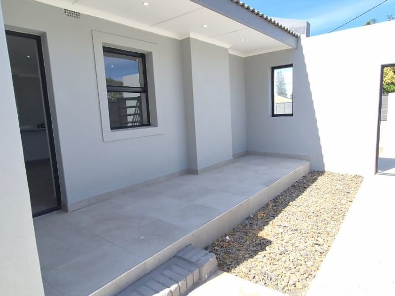 A clean, modern covered patio area featuring neutral tiled flooring, recessed lighting, and contemporary aluminium window and door frames.