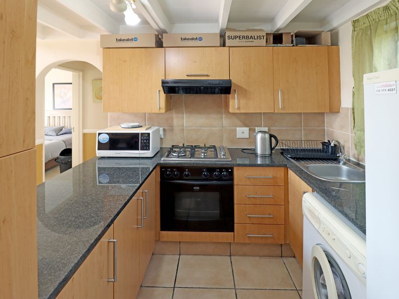 A functional kitchen featuring light wood cabinetry, granite countertops, a gas hob, built-in oven, and tiled finishes with exposed ceiling beams.