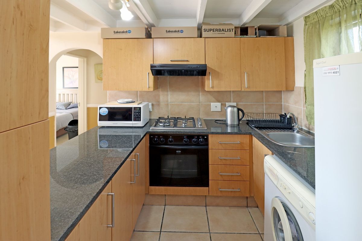 A functional kitchen featuring light wood cabinetry, granite countertops, a gas hob, built-in oven, and tiled finishes with exposed ceiling beams.