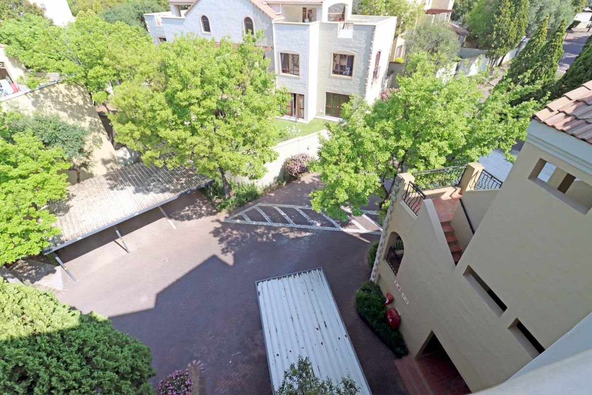An elevated aerial view of the apartment complex grounds, featuring paved parking areas, carports, and surrounding landscaped greenery.