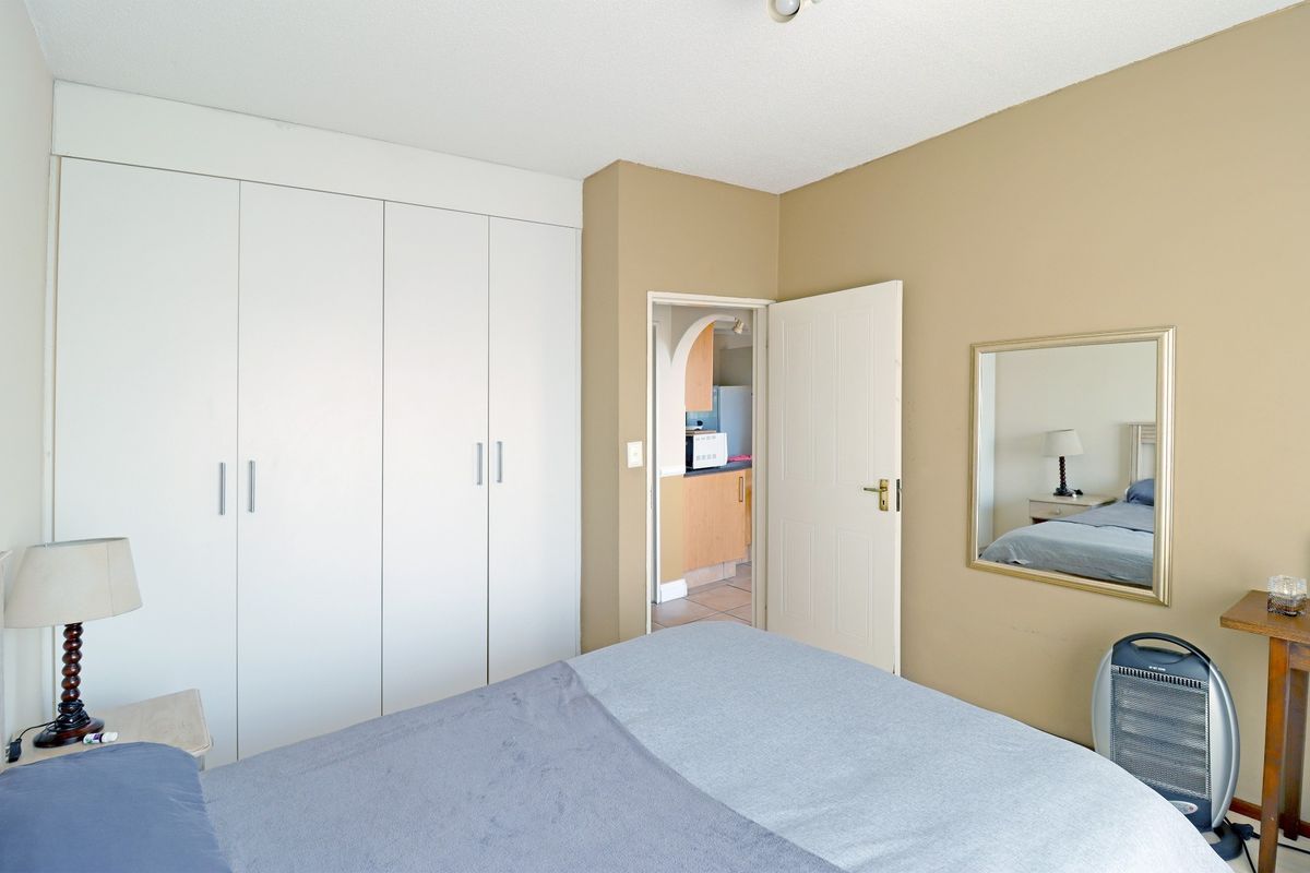 A bedroom featuring built-in white cupboards, neutral wall tones, and an internal doorway leading to an adjacent kitchen area.