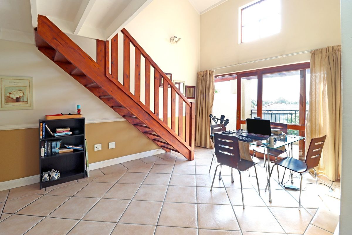 Open-plan living area featuring a wooden staircase, tiled flooring, and large sliding glass doors leading to a balcony with natural light.
