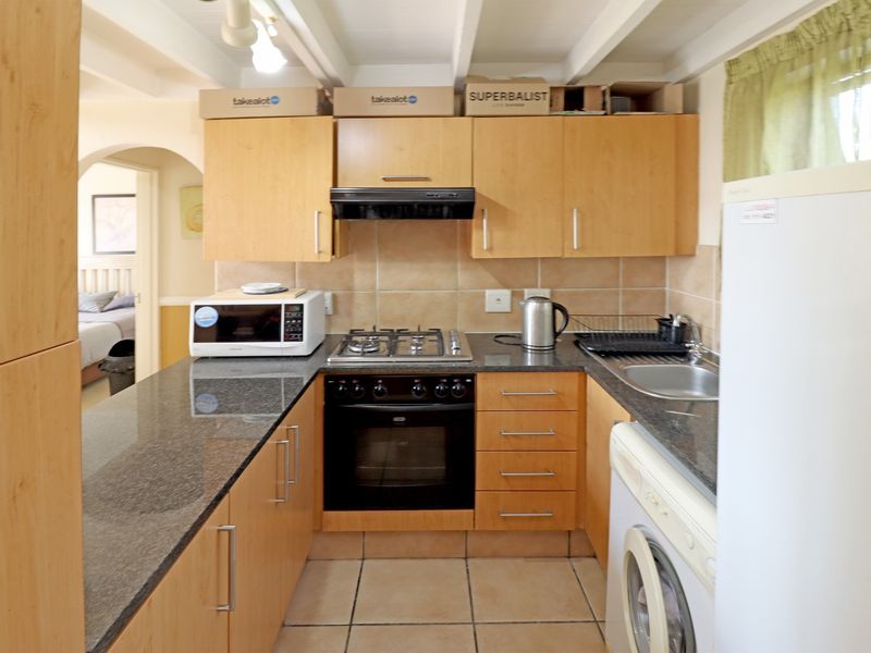 Compact kitchen featuring light wood cabinetry, granite countertops, built-in gas hob, electric oven, and tiled flooring with exposed ceiling beams.