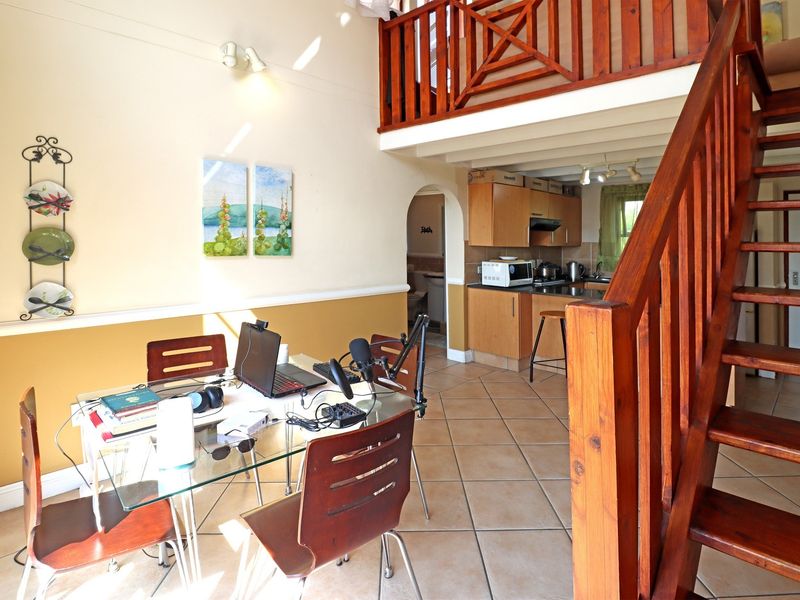 Open plan living and dining area featuring a wooden staircase leading to a mezzanine level, adjacent to a functional kitchen with tiled flooring.