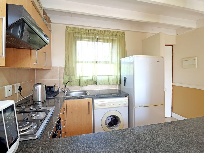 Compact kitchen featuring laminate cabinetry, granite countertops, a gas hob with extractor, and integrated space for a washing machine.
