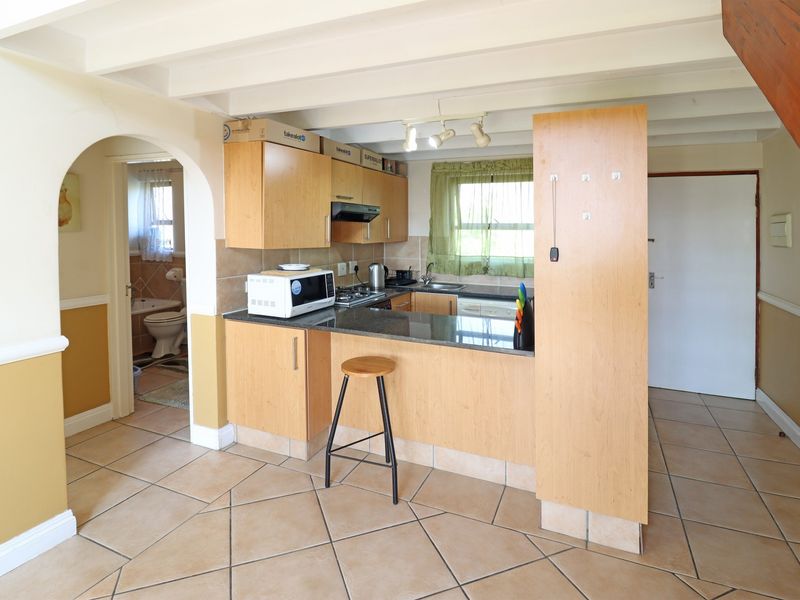 Open-plan kitchen featuring light wood cabinetry, granite countertops, and tiled flooring, with an adjacent archway leading to the bathroom area.