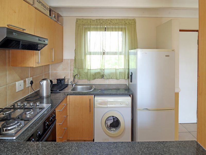 Compact kitchen featuring granite countertops, built-in cabinetry, a gas hob with extractor fan, and integrated space for a washing machine.