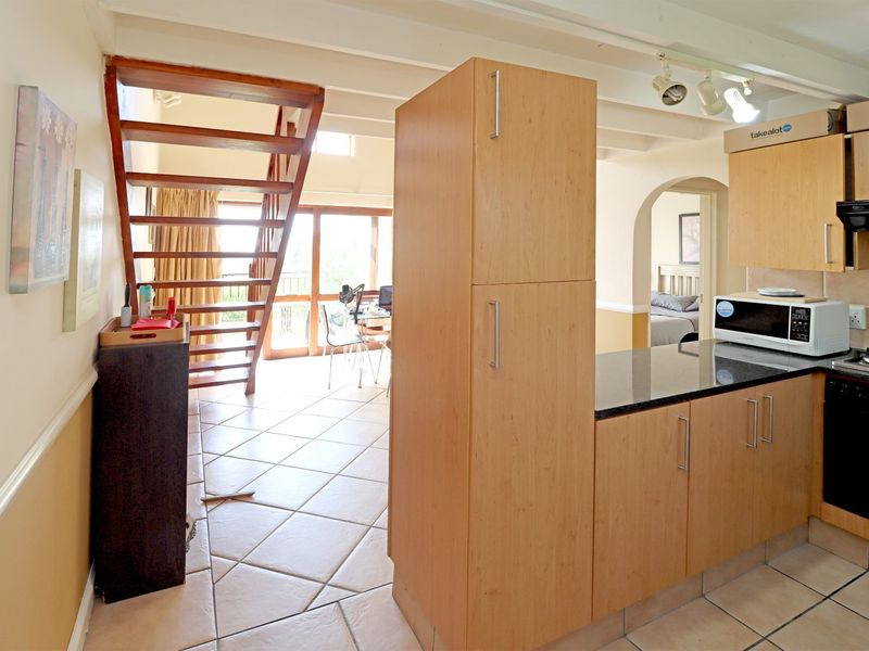 Open-plan kitchen and living area featuring tiled floors, wooden staircase, exposed ceiling beams, and functional kitchen cabinetry with granite countertops.