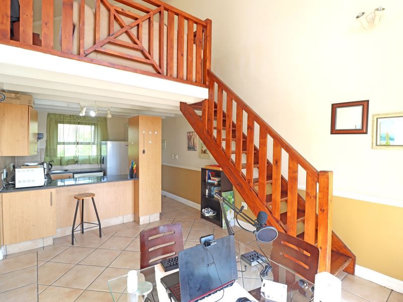 Open plan living area featuring a kitchen with wooden cabinetry, tiled floors, and a wooden staircase leading to a mezzanine level.