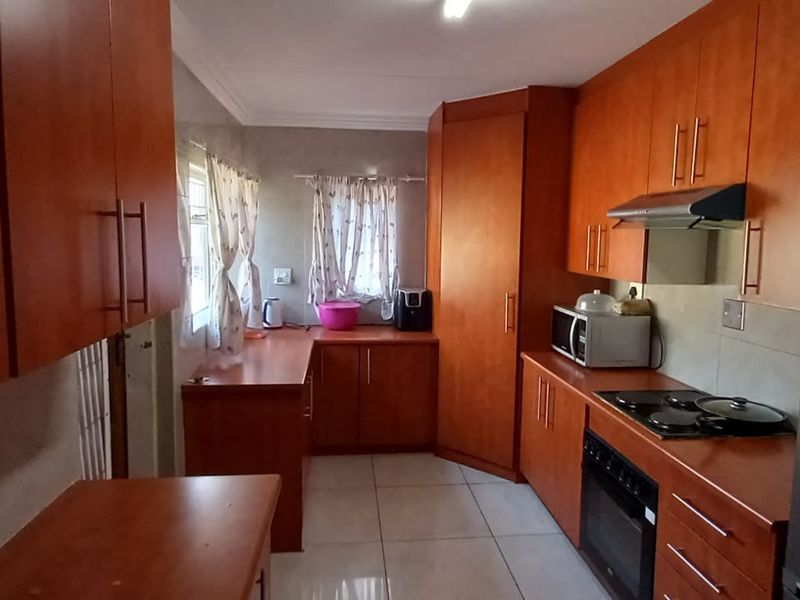 A functional kitchen featuring warm-toned wooden cabinetry, tiled flooring, a built-in oven, and an electric hob with an extractor fan.