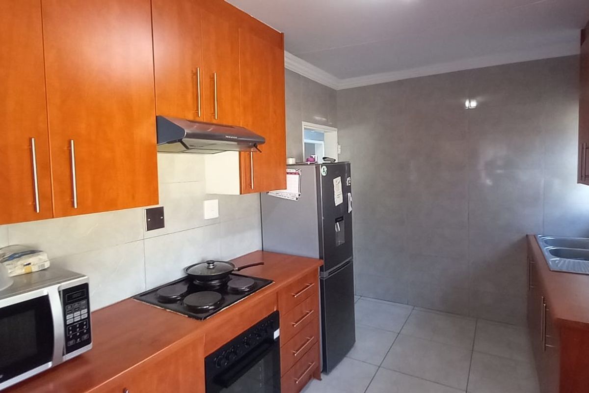 A functional kitchen featuring warm-toned wooden cabinetry, a built-in electric hob with extractor fan, and a double sink with tiled finishes.