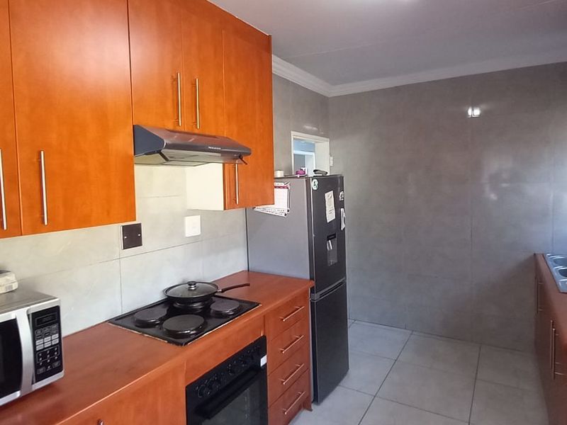 A functional kitchen featuring warm-toned wooden cabinetry, a built-in electric hob with extractor fan, and a double sink with tiled finishes.