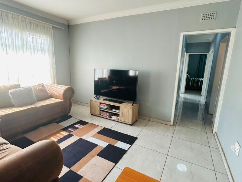 A bright living room featuring neutral wall tones, tiled flooring, and a clear transition into the hallway area.