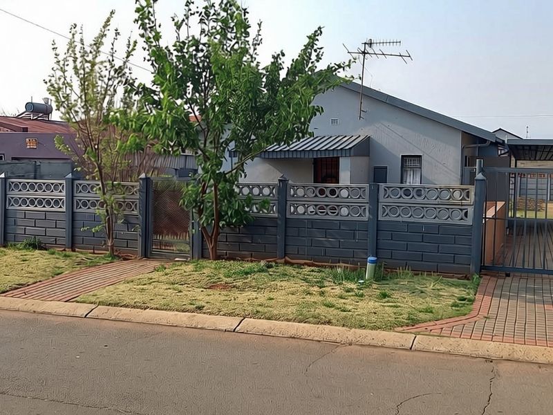 Front view of a residential property featuring a secure perimeter wall, metal gate, paved driveway, and a covered carport.