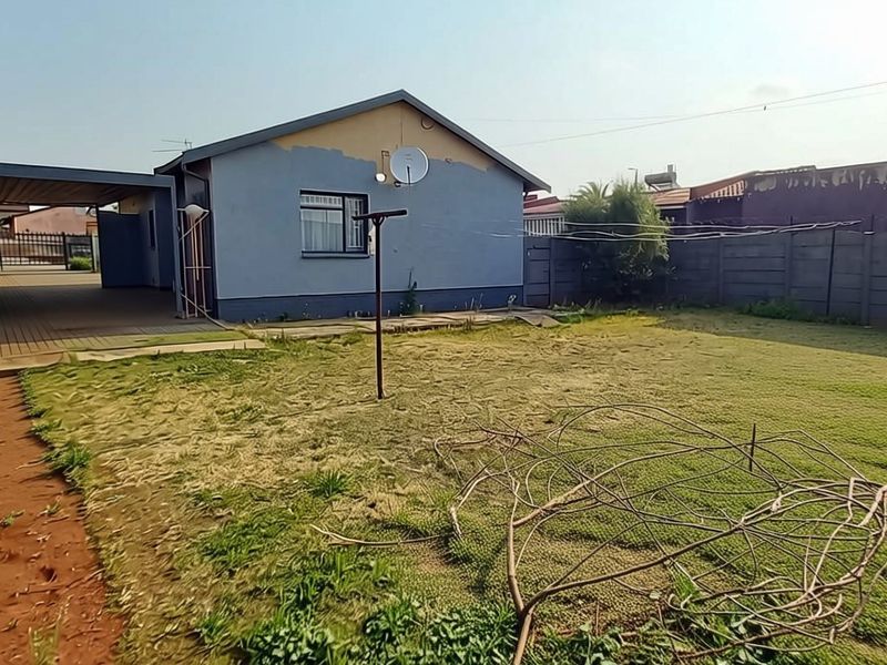 Rear view of the property featuring a spacious backyard, precast concrete boundary walls, and a covered patio area.