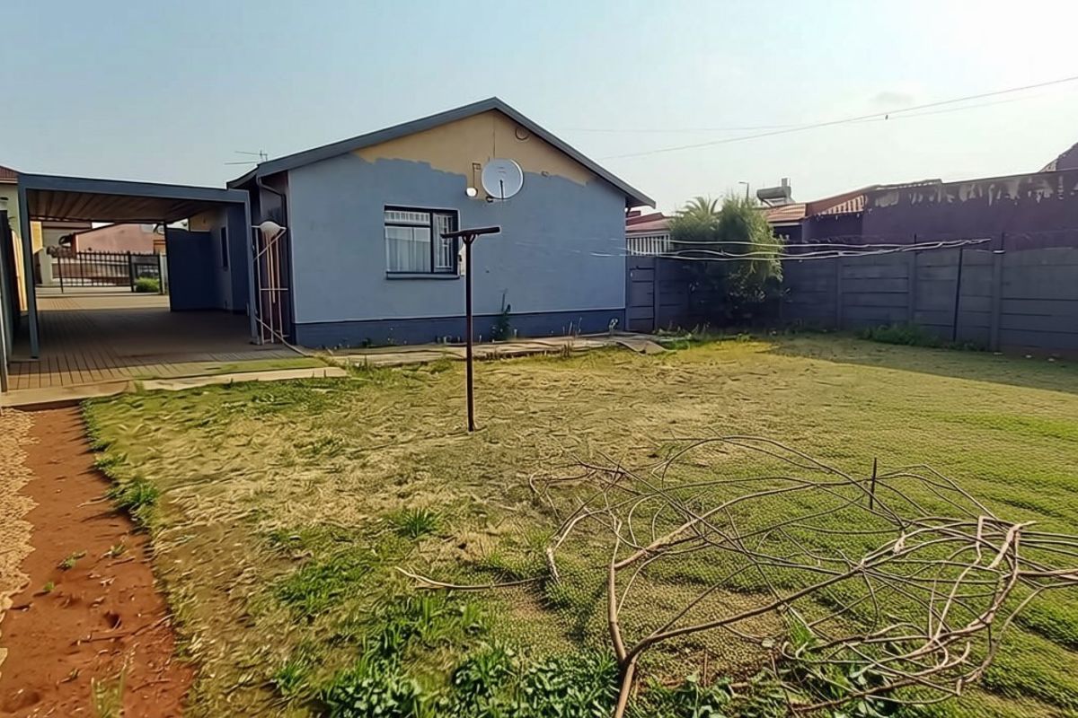 Rear view of the property featuring a spacious backyard, precast concrete boundary walls, and a covered patio area.