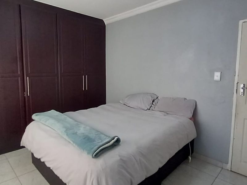 A bedroom featuring dark wood built-in cupboards, tiled flooring, and neutral wall finishes.