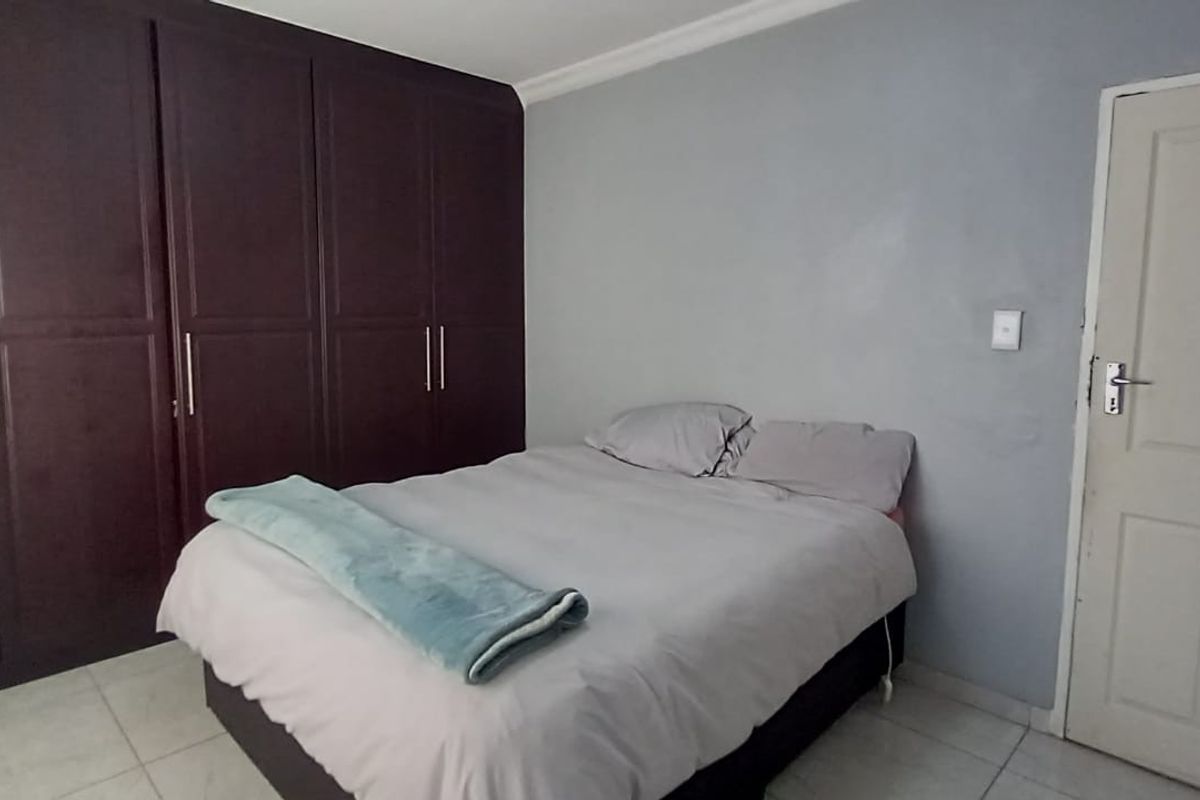 A bedroom featuring dark wood built-in cupboards, tiled flooring, and neutral wall finishes.