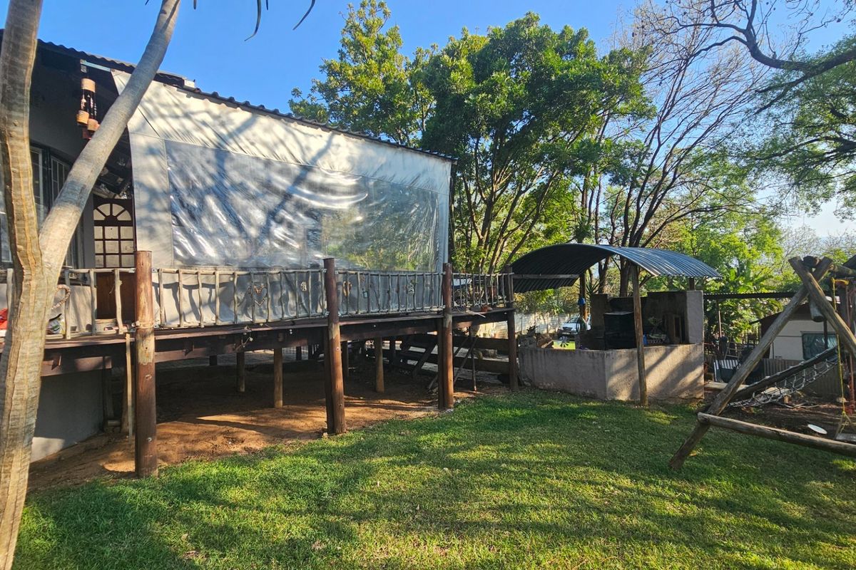 Rear exterior view featuring a raised timber deck with protective weather blinds and a built-in masonry braai area set within a garden.