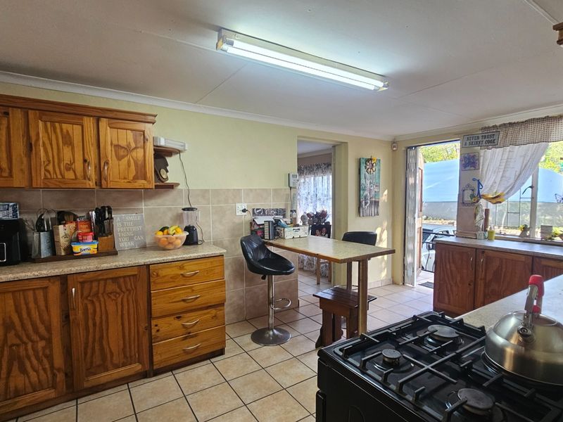 A functional kitchen featuring wooden cabinetry, tiled backsplash, and a gas hob, with direct access to an outdoor area.