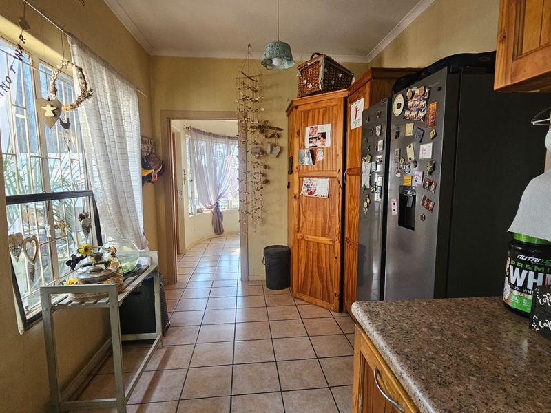 A functional kitchen area featuring tiled flooring, built-in wooden cabinetry, and laminate countertops, leading through to an adjacent living space.