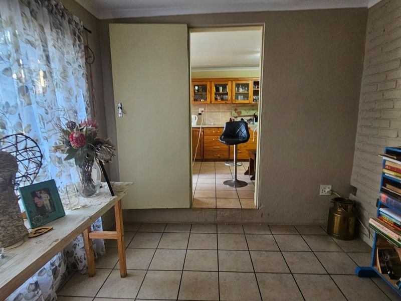 A living area featuring tiled flooring and a painted brick wall, with a doorway leading through to the kitchen.