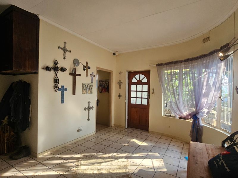 A living area featuring tiled flooring, a curved window, and a timber entrance door, offering a functional space with potential for modernization.