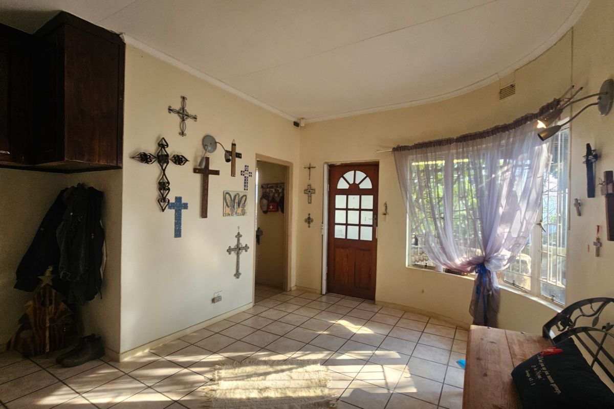 A living area featuring tiled flooring, a curved window, and a timber entrance door, offering a functional space with potential for modernization.