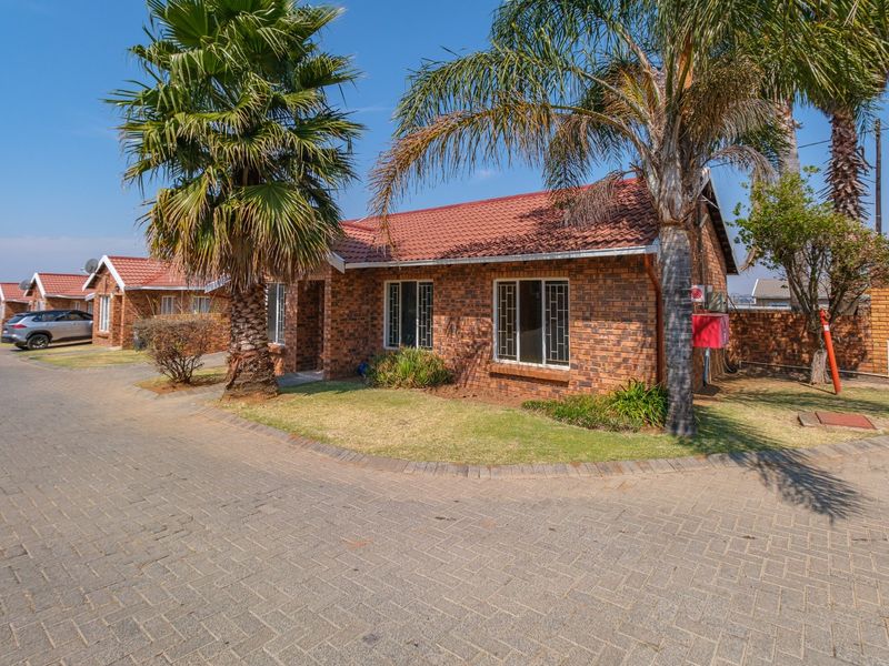 A well-maintained face brick townhouse featuring a tiled roof, paved driveway, and established garden in a secure complex setting.