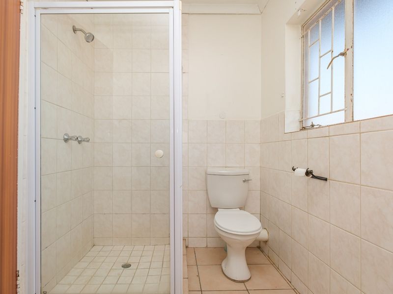 A functional bathroom featuring a shower enclosure, toilet, and neutral wall tiling. The space is ready for cosmetic updates to modernize the finishes.