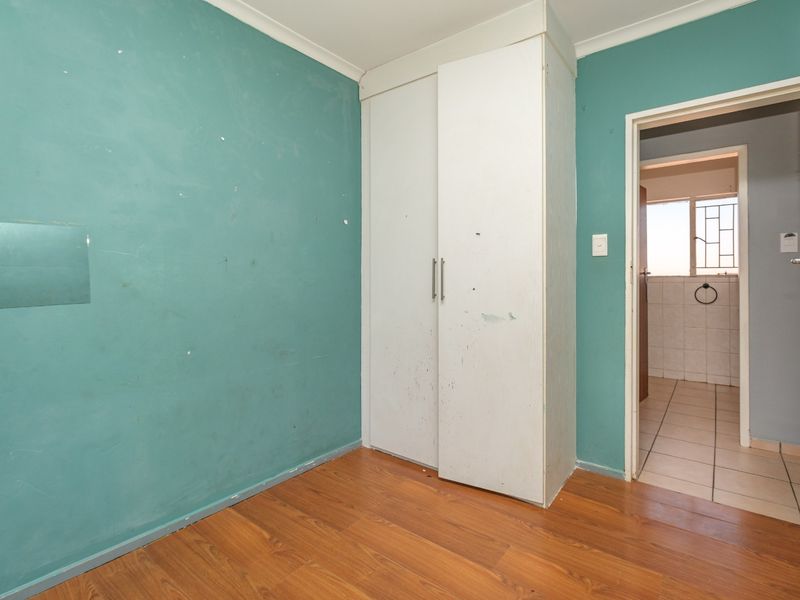 An empty bedroom featuring laminate flooring and a built-in wardrobe, requiring cosmetic updates to the wall finishes and cabinetry.