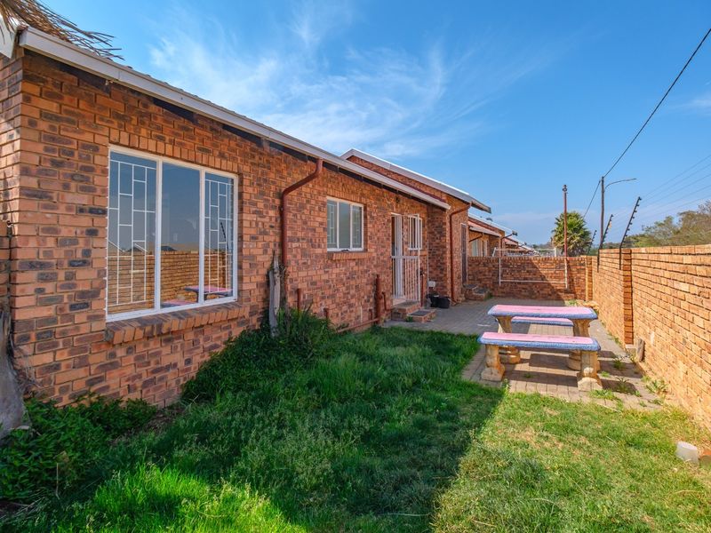 Rear exterior view of the townhouse featuring a face brick facade, paved patio area, and enclosed garden with perimeter security fencing.