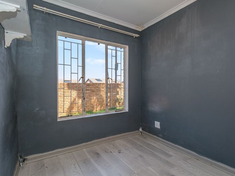 An empty bedroom featuring laminate flooring, dark grey walls, and security bars on the window, requiring cosmetic updates and maintenance.