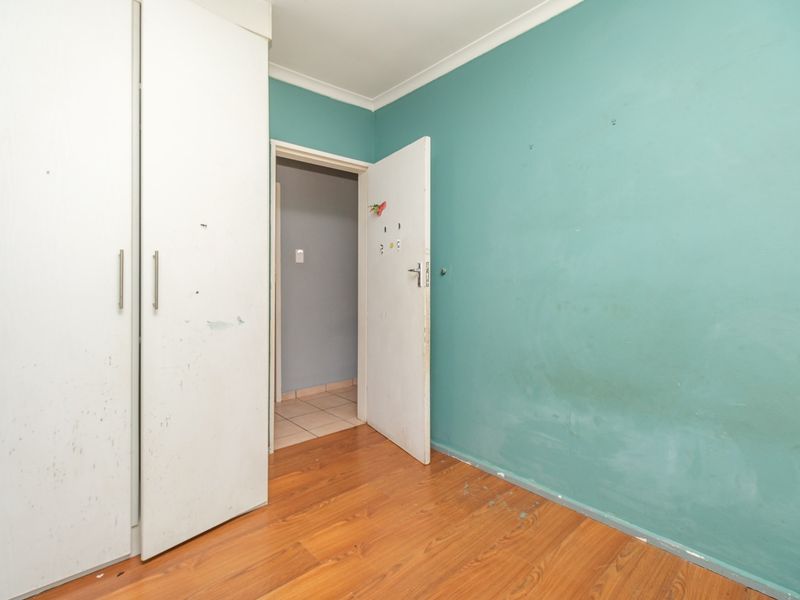 An empty bedroom featuring built-in cupboards, laminate flooring, and teal-painted walls, requiring cosmetic updates to restore its appeal.