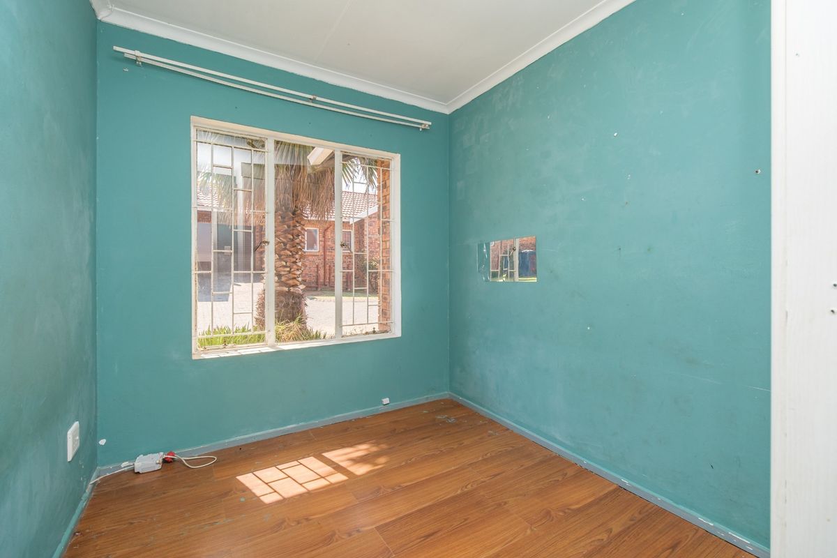 An empty bedroom featuring laminate flooring, security bars on the window, and teal-painted walls in need of cosmetic attention.