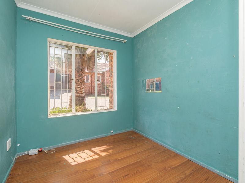 An empty bedroom featuring laminate flooring, security bars on the window, and teal-painted walls in need of cosmetic attention.