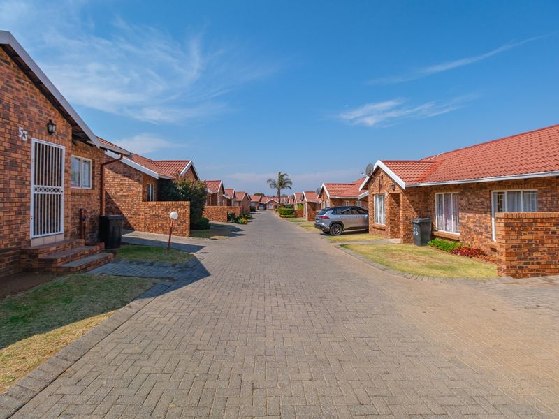 A view of the residential townhouse complex street, featuring uniform face brick architecture, tiled roofs, and paved driveway access.