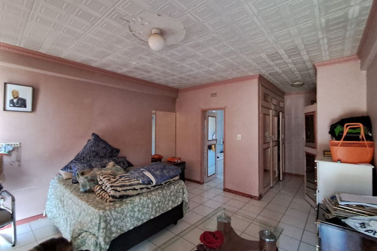 Spacious bedroom featuring built-in cupboards, tiled flooring, and a textured ceiling. The room requires cosmetic updates to improve its overall condition and appeal.