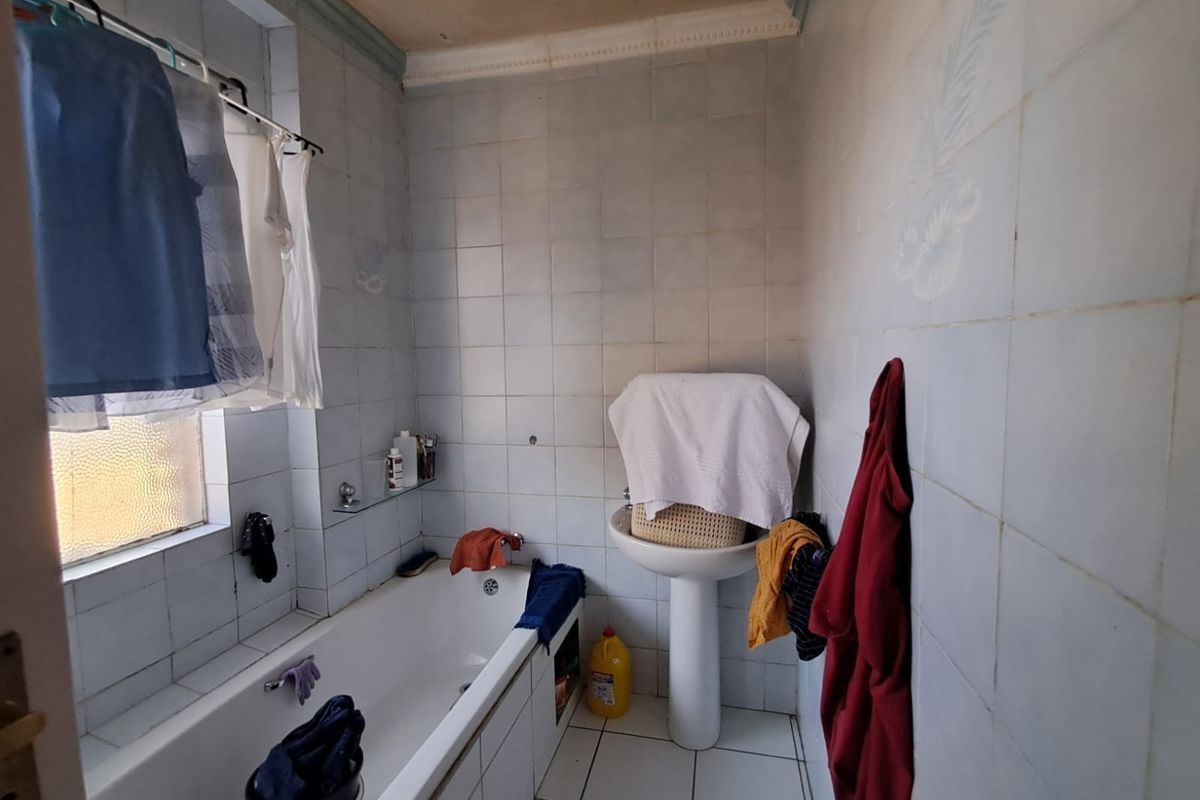 A dated bathroom featuring a pedestal basin and built-in bathtub with full-height wall tiling, requiring cosmetic updates and maintenance to the ceiling and finishes.