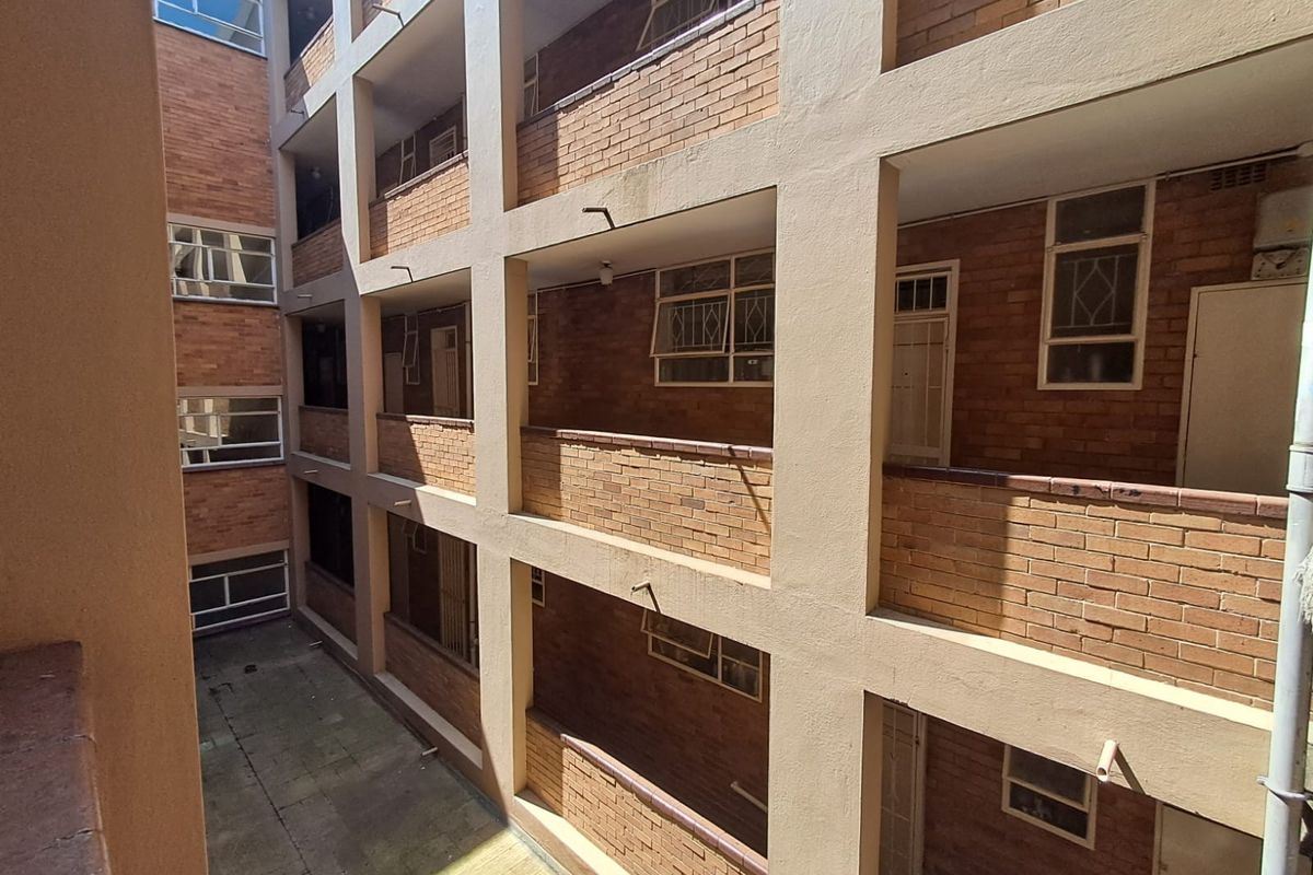 Exterior view of an apartment complex featuring multi-level brick walkways and access corridors with security gates and casement windows.