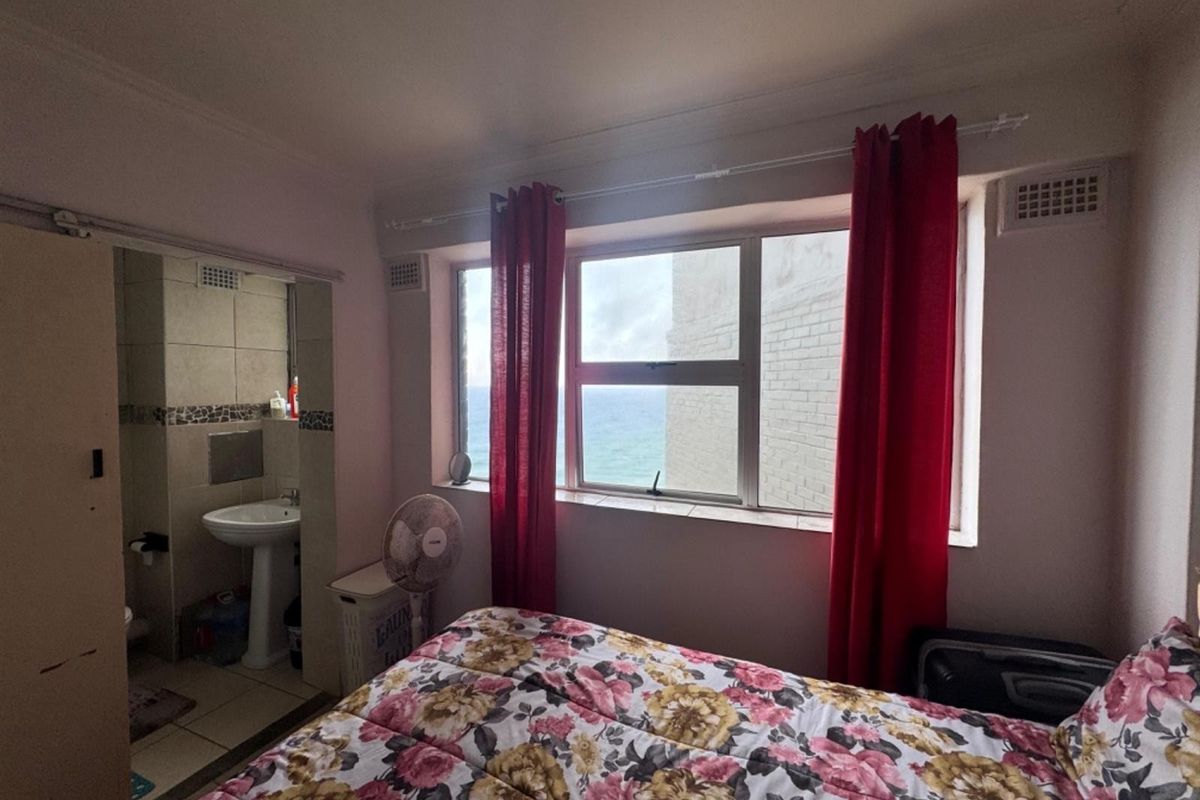 A bedroom featuring an en-suite bathroom with a pedestal basin and tiled finishes, complemented by a window offering a partial sea view.