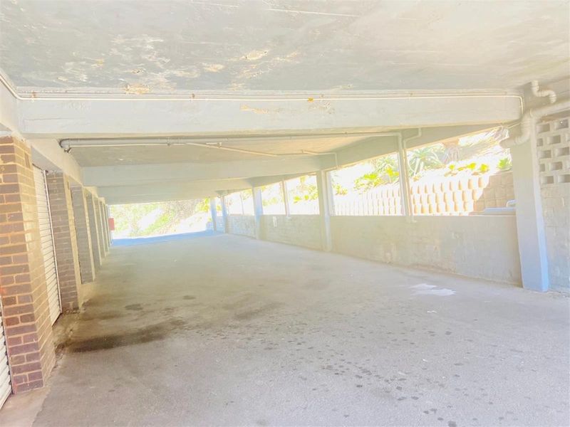 A covered parking area or garage featuring concrete ceilings, brick structural pillars, and a retaining wall, showing signs of wear and surface deterioration.