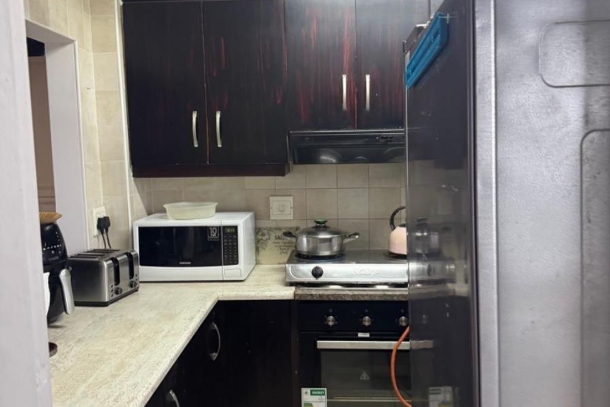 Compact kitchen featuring dark wood cabinetry, laminate countertops, built-in oven, gas hob, and tiled backsplash in a functional layout.