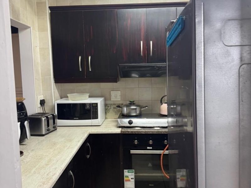 Compact kitchen featuring dark wood cabinetry, laminate countertops, built-in oven, gas hob, and tiled backsplash in a functional layout.