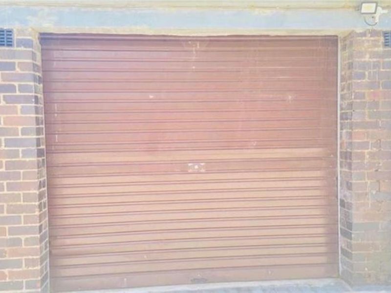 A standard brick-constructed garage featuring a brown roller door and external drainage pipe.