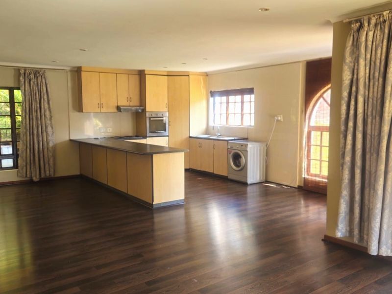Spacious open-plan living and kitchen area featuring laminate flooring, light wood cabinetry, integrated oven, and large windows providing ample natural light.