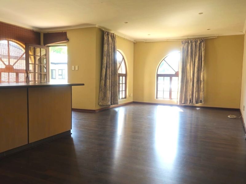 Spacious open-plan living area featuring dark laminate flooring, distinctive arched windows, and a built-in breakfast bar, offering a bright and versatile layout.
