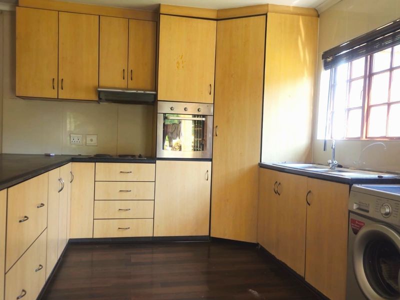 A functional kitchen featuring light wood-tone cabinetry, built-in oven, extractor fan, and dark laminate countertops with integrated sink and laundry plumbing connections.