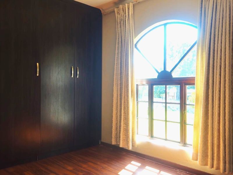 A bright bedroom featuring dark wood built-in wardrobes, timber flooring, and a distinctive arched window with natural light.
